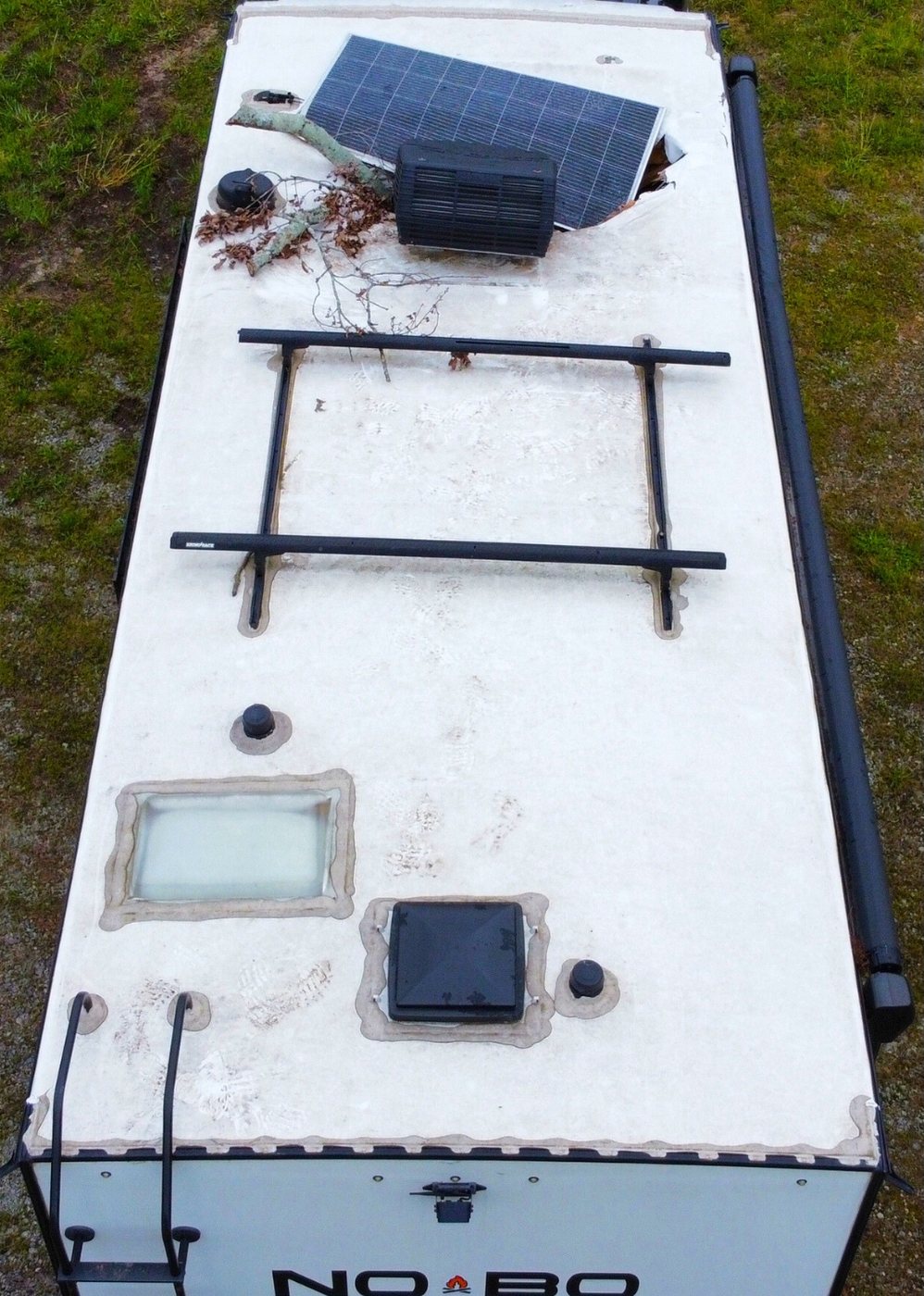 Tree branch resting on an RV roof beside a solar panel punched through the membrane